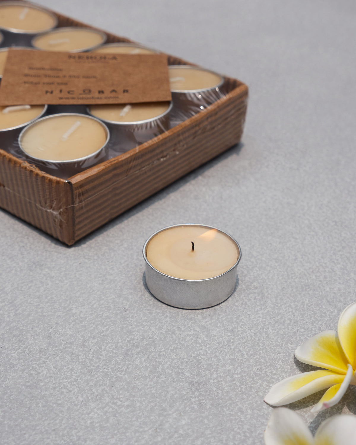 Lit Nerola tealight in a silver cup with the packaged set behind it.