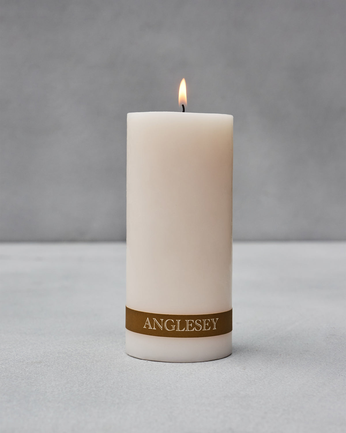 Lit Anglesey Pillar Candle with its gold ANGLESEY label band.