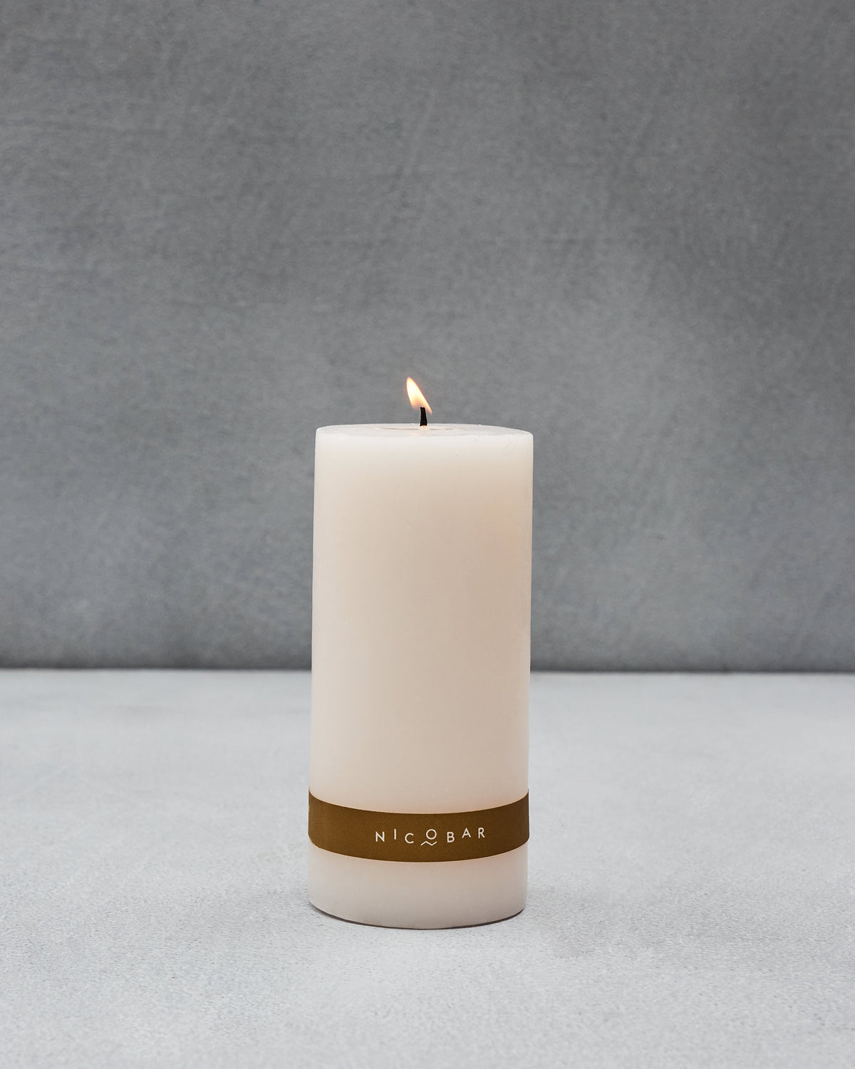 Lit Anglesey Pillar Candle with a gold label band.