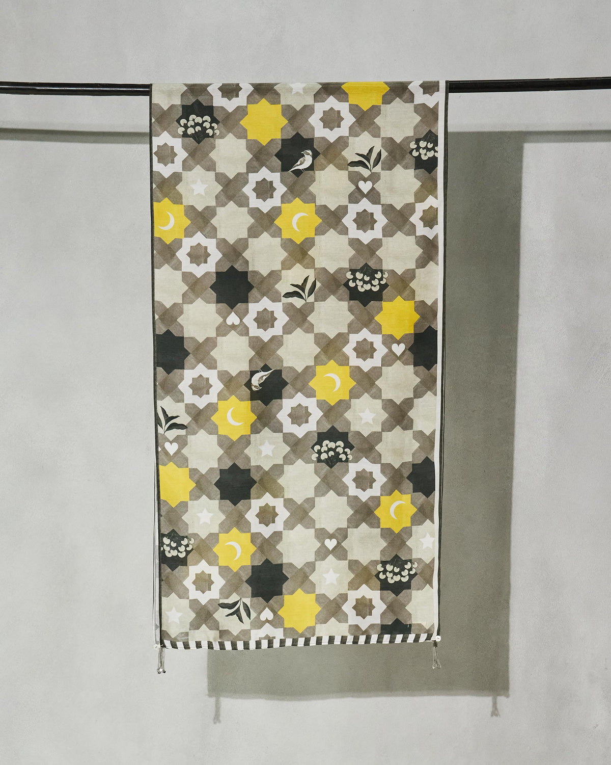 Full Celeste scarf hung from a rod, grey and yellow star tiles with small birds.
