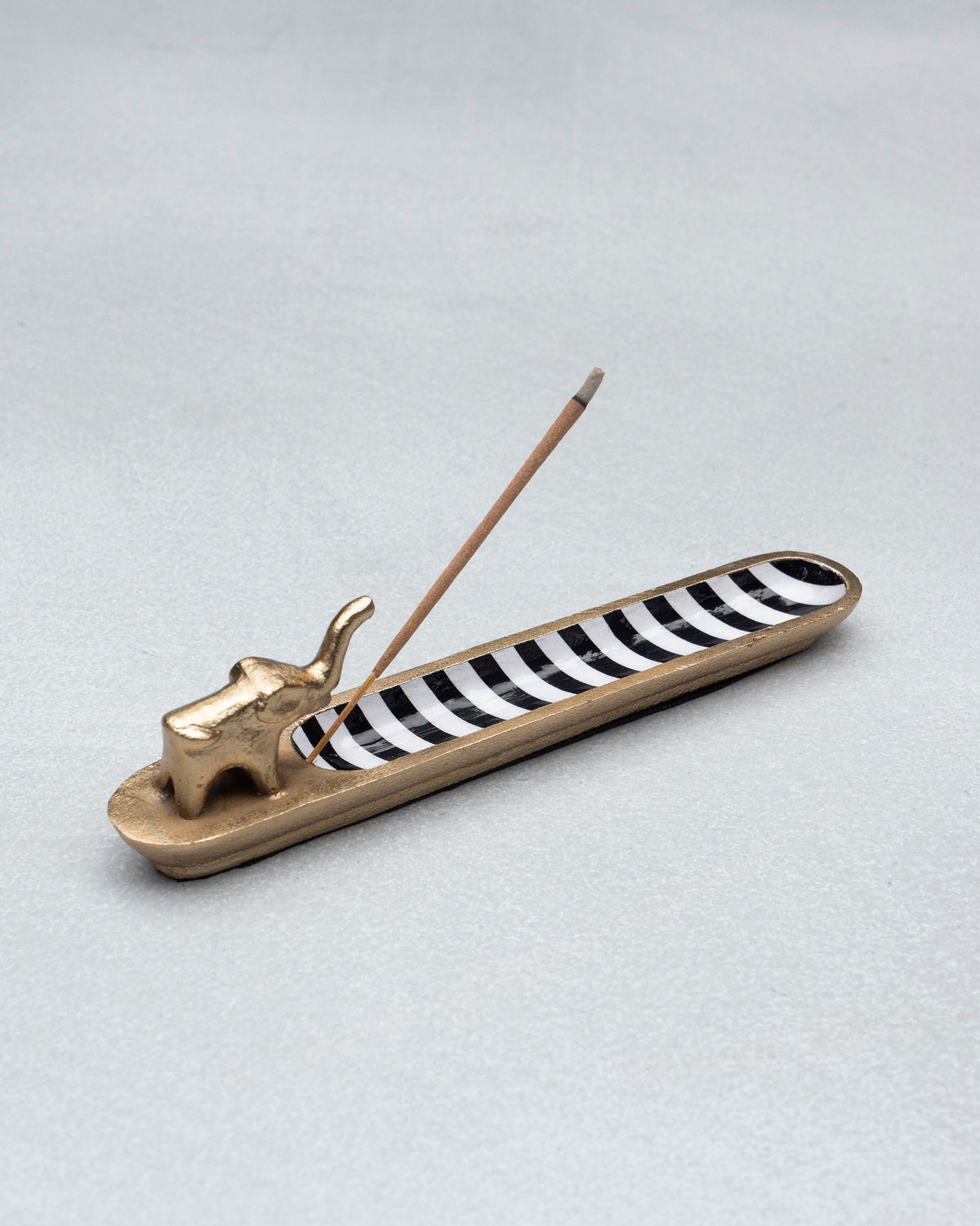 Gold Haathi incense holder with a lit incense stick over the striped tray.