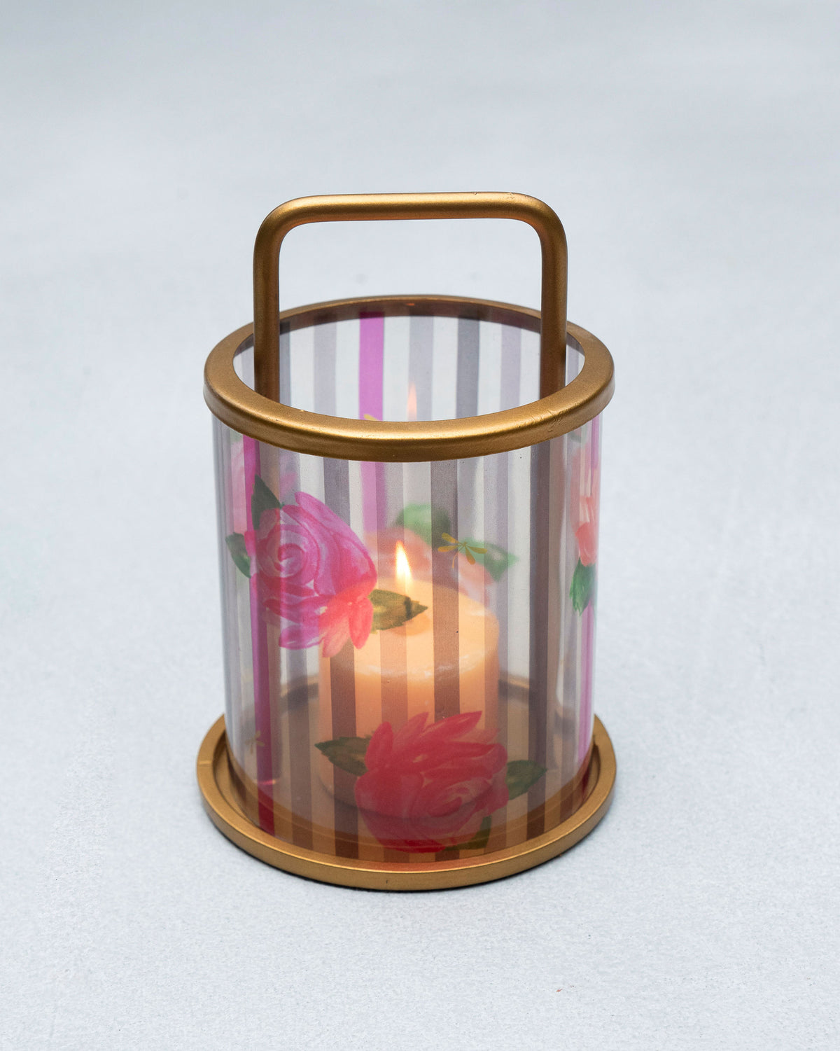 Striped Roses glass lantern with gold handle and a lit pillar candle.