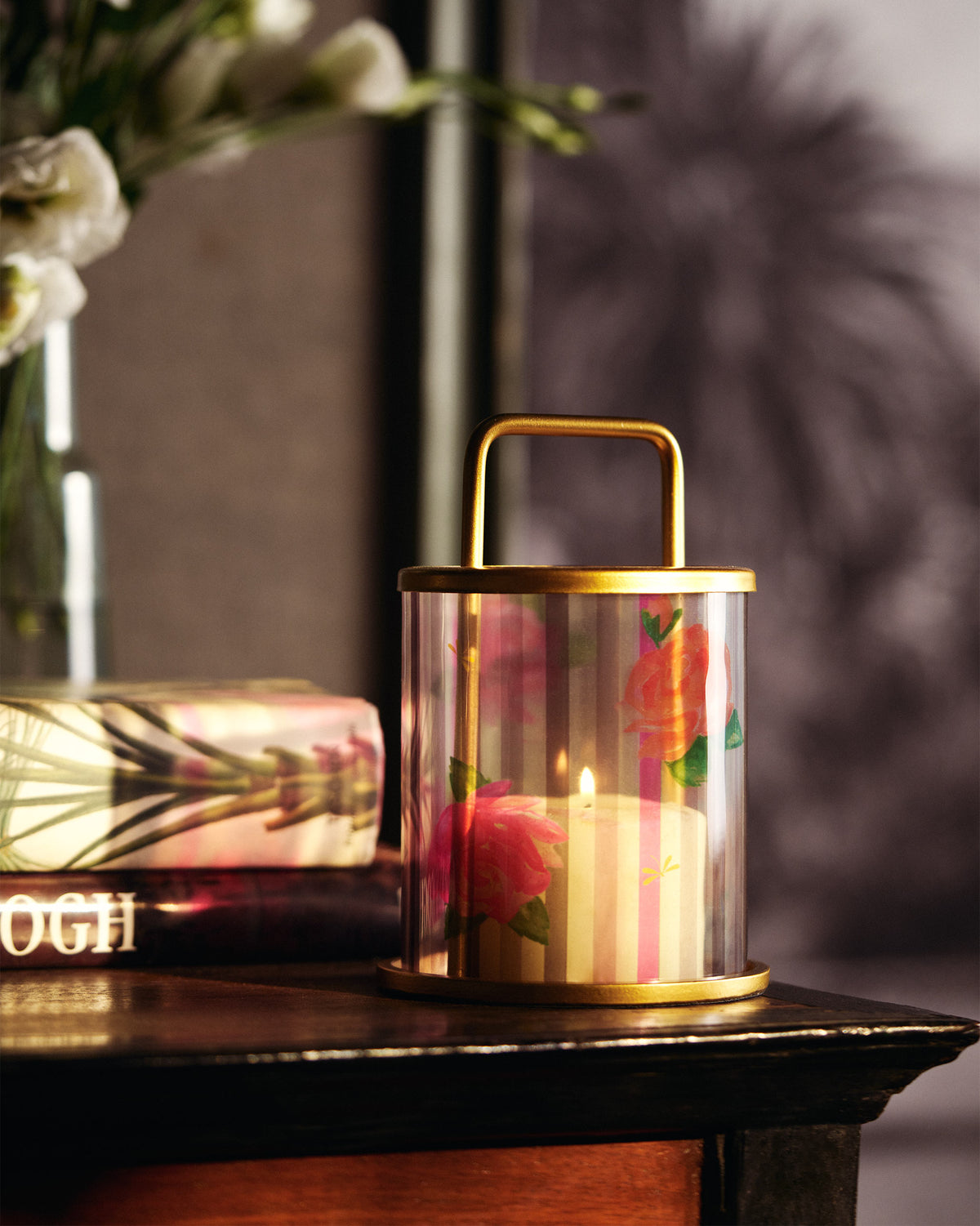 Lit Striped Roses lantern with pink roses glowing on a wooden table.