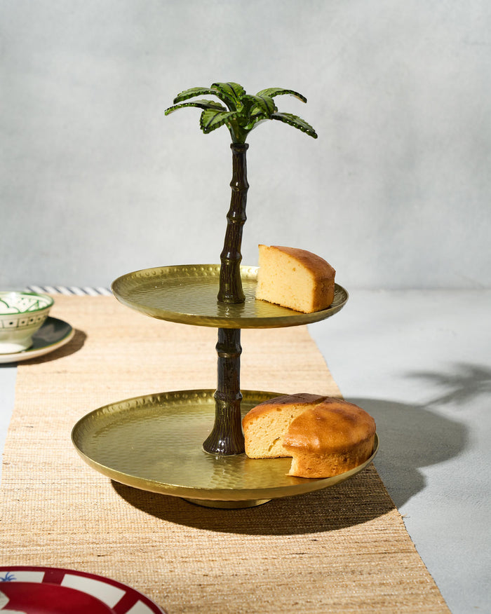Two-tier Gilded Palm cake stand with hammered brass trays and a green palm topper.