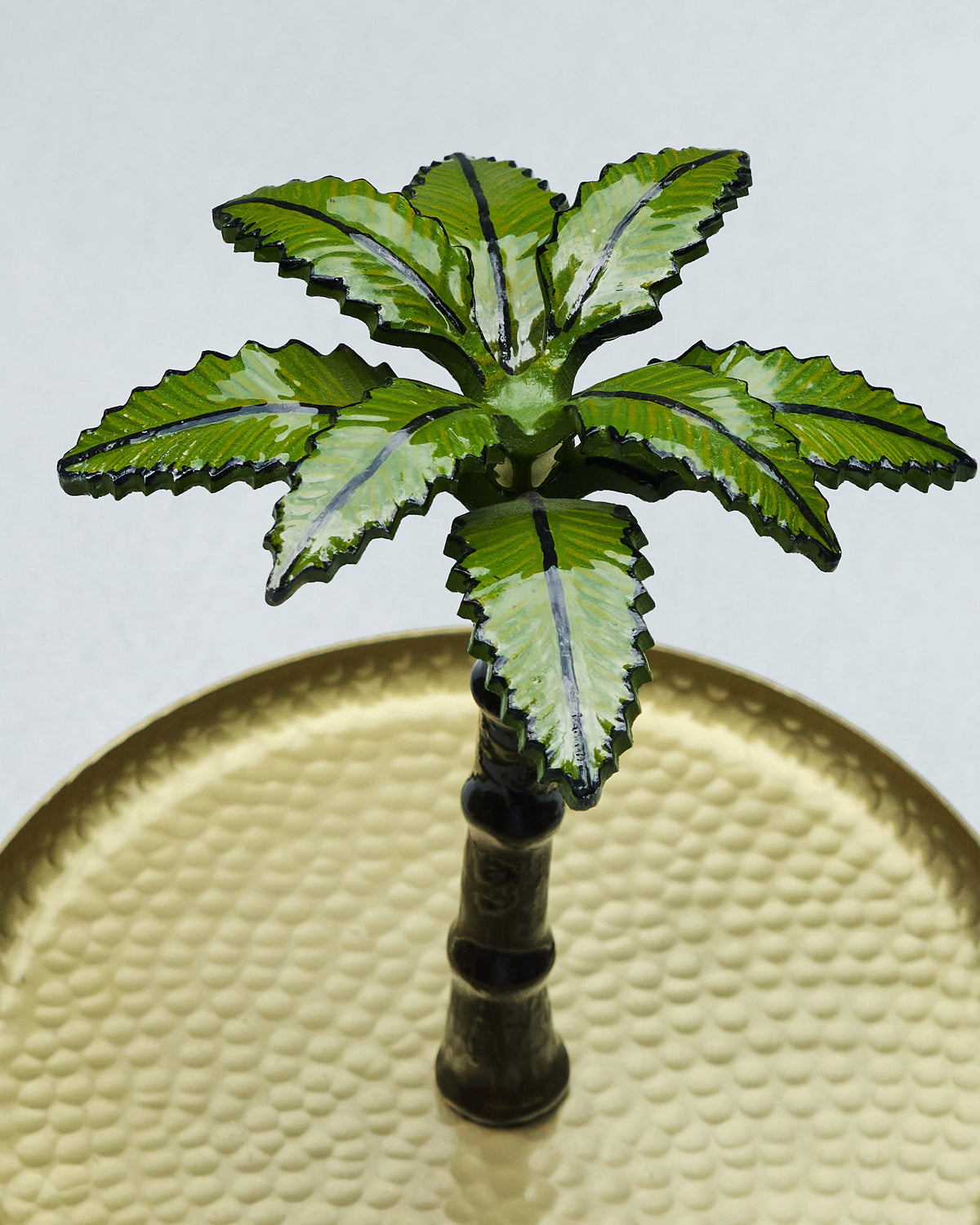 Close-up of the green palm topper on a hammered brass Gilded Palm cake stand.