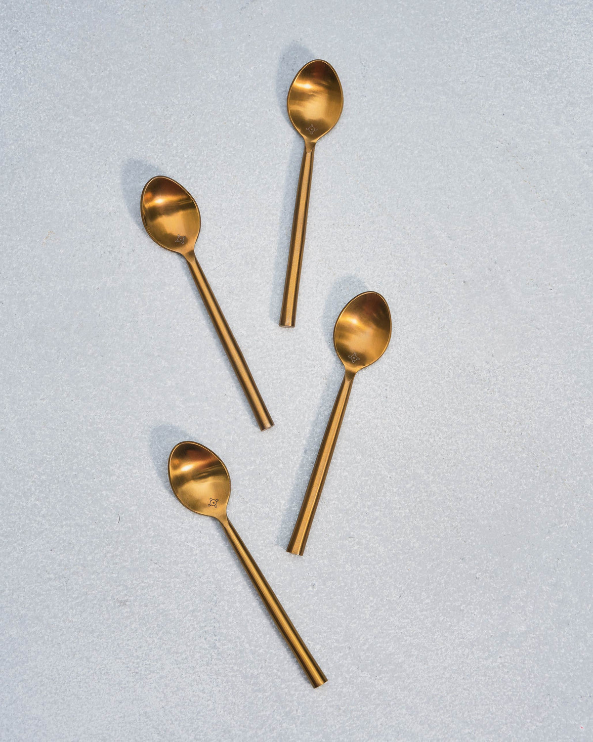 Four gold Sahara dessert spoons with slim handles scattered on a surface.
