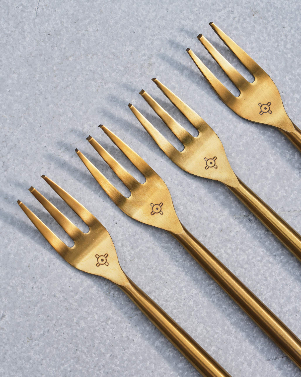 Close-up of gold Sahara forks showing three tines and a neck emblem.