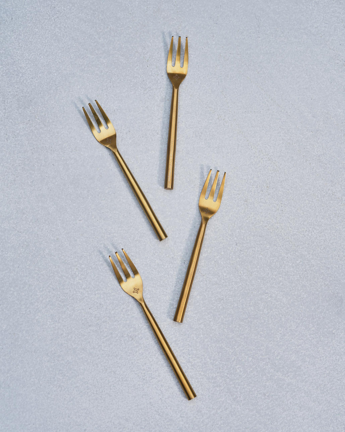 Four gold Sahara dessert forks scattered on a grey surface.