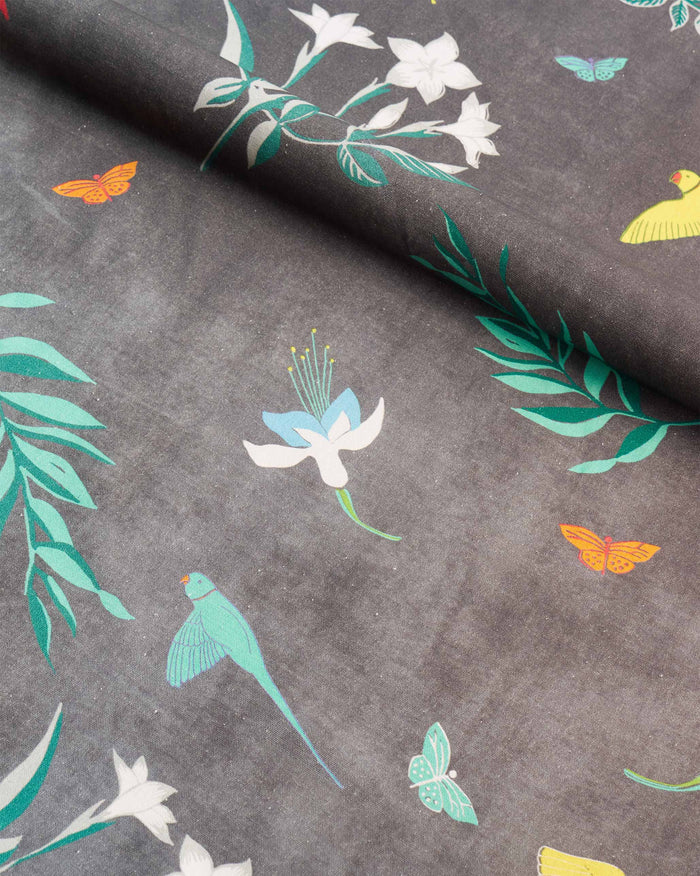 Close-up of Botanical Fabric in grey showing flowers, butterflies and parrots.