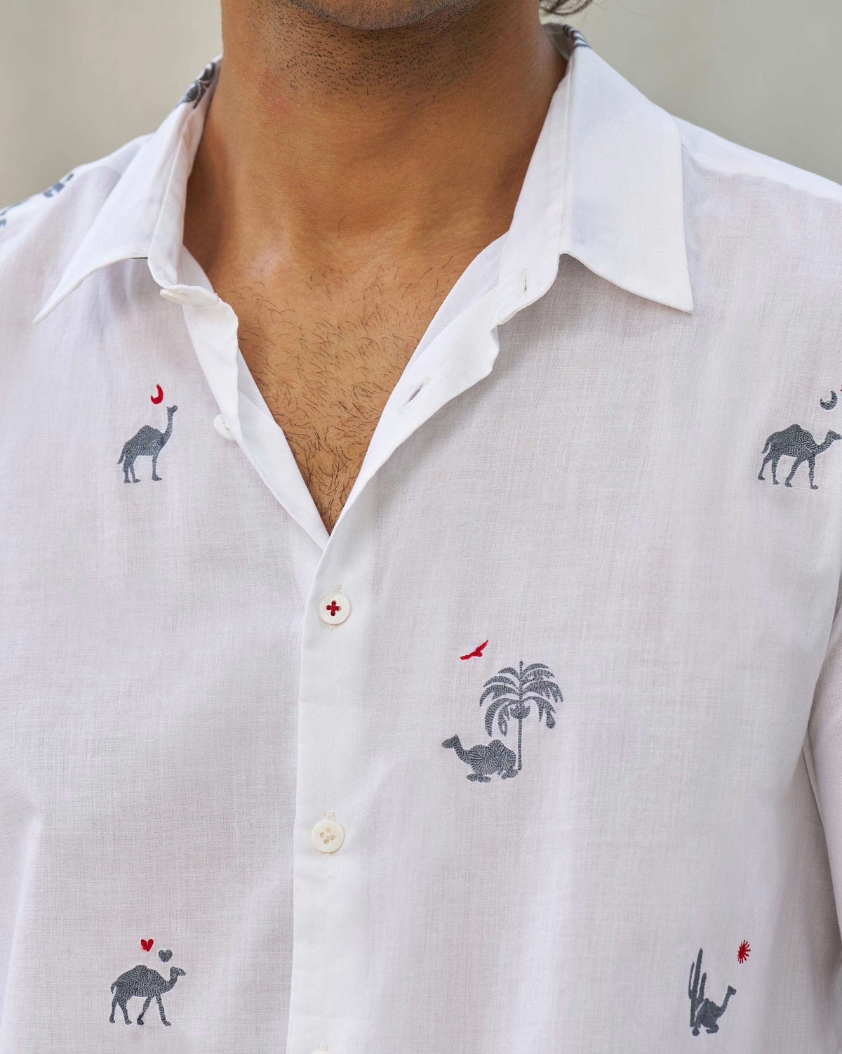 Close-up of a white Hakuna shirt showing camel motifs and a red-stitched button.