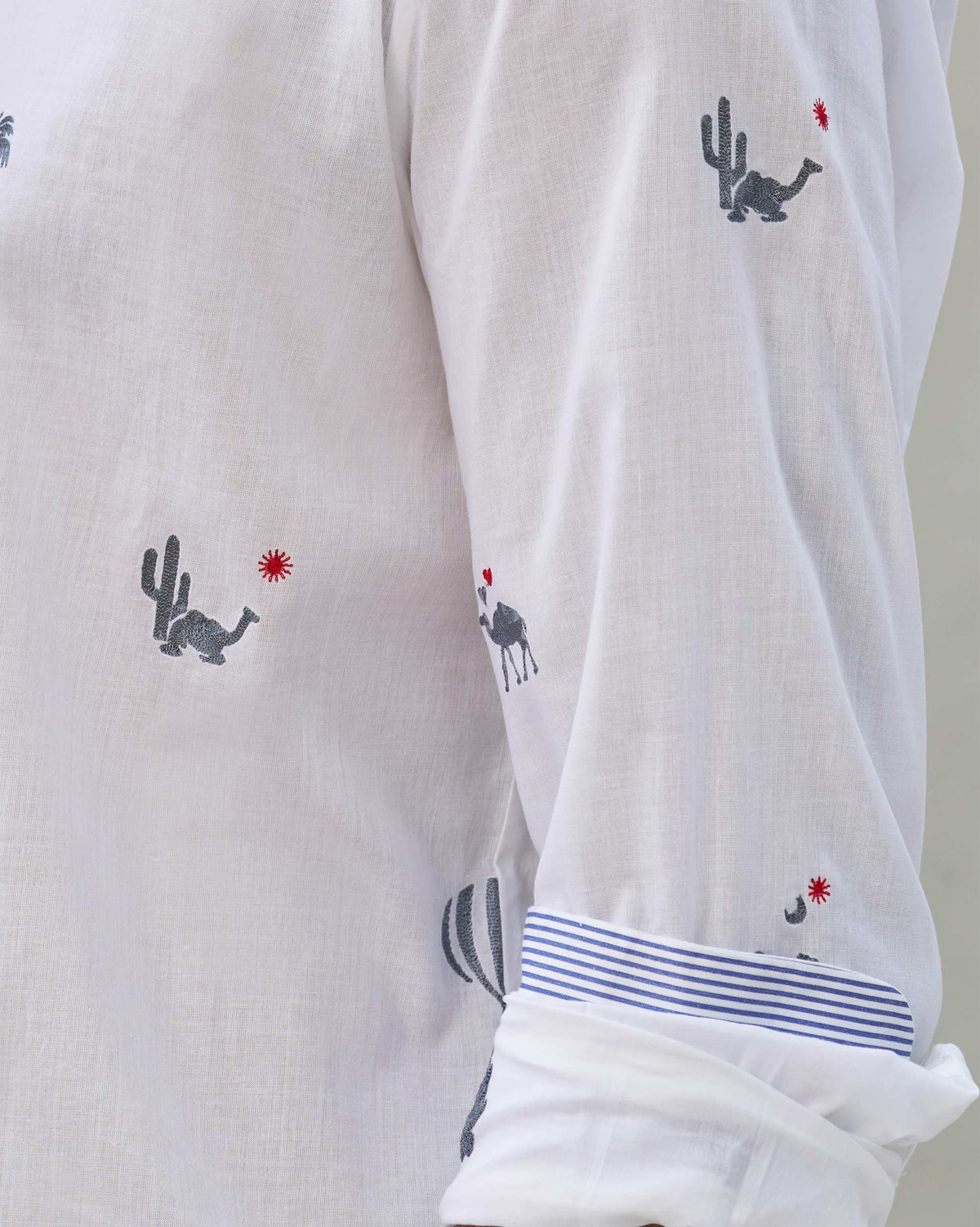 Close-up of camel motifs and blue striped cuff lining on a white Hakuna shirt.