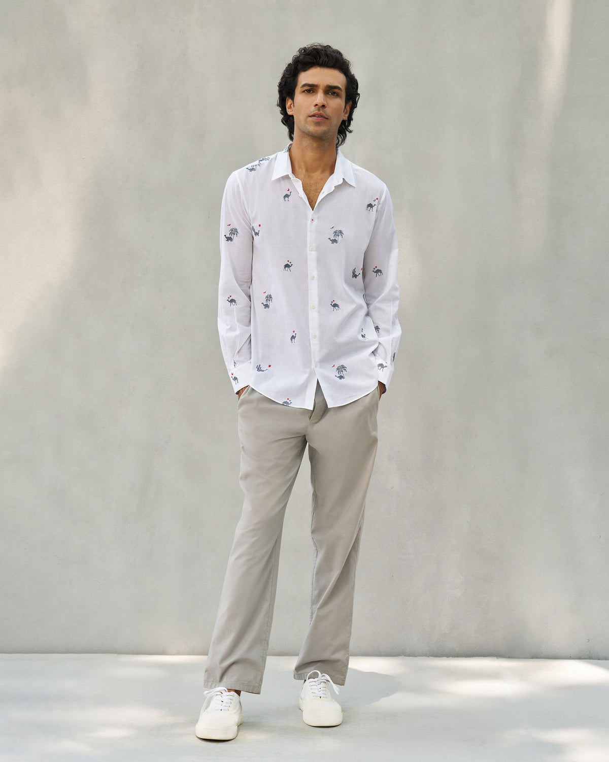 Person wearing a white Hakuna shirt with camel motifs over beige trousers.