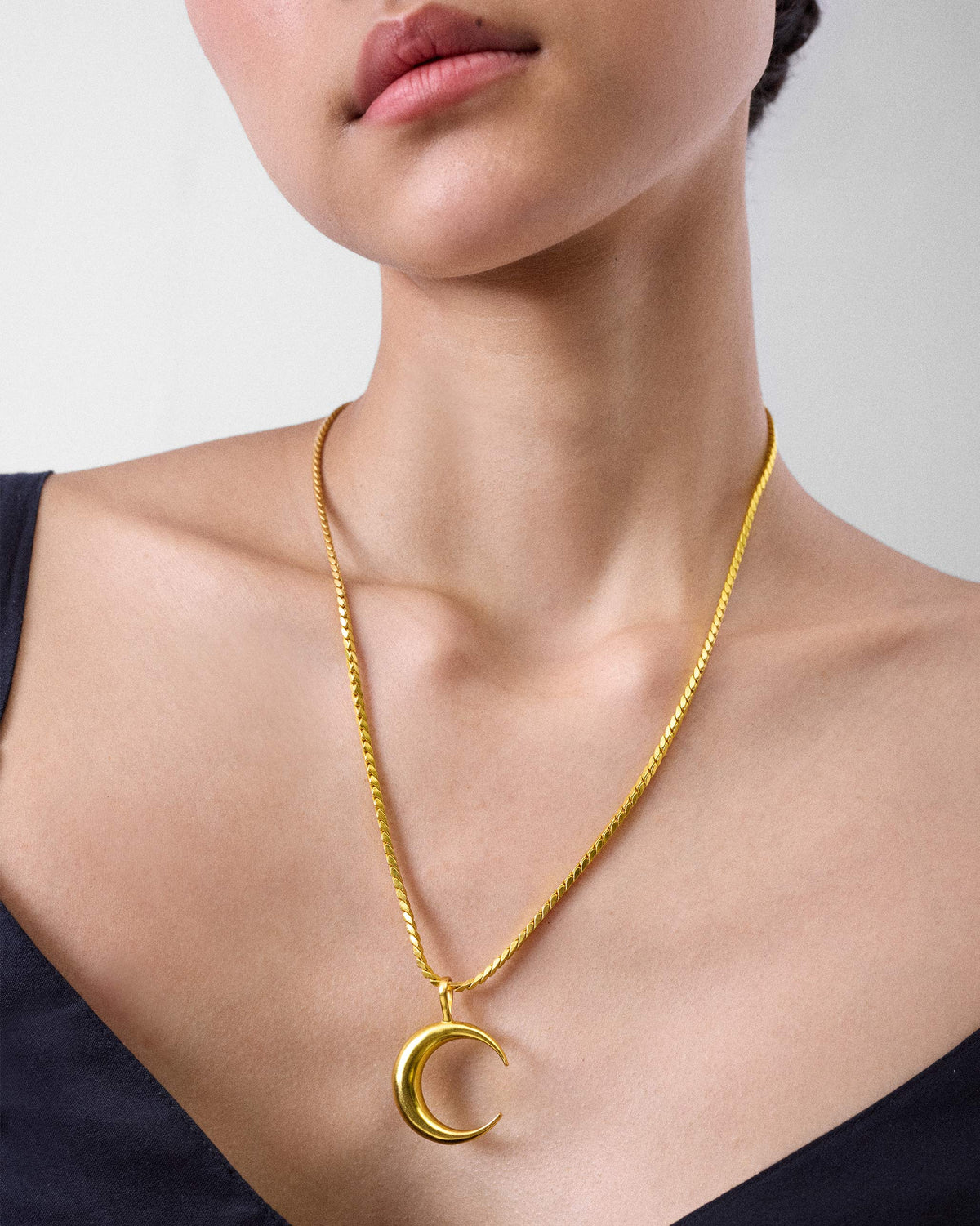 Gold crescent Moonfall pendant on a textured chain.