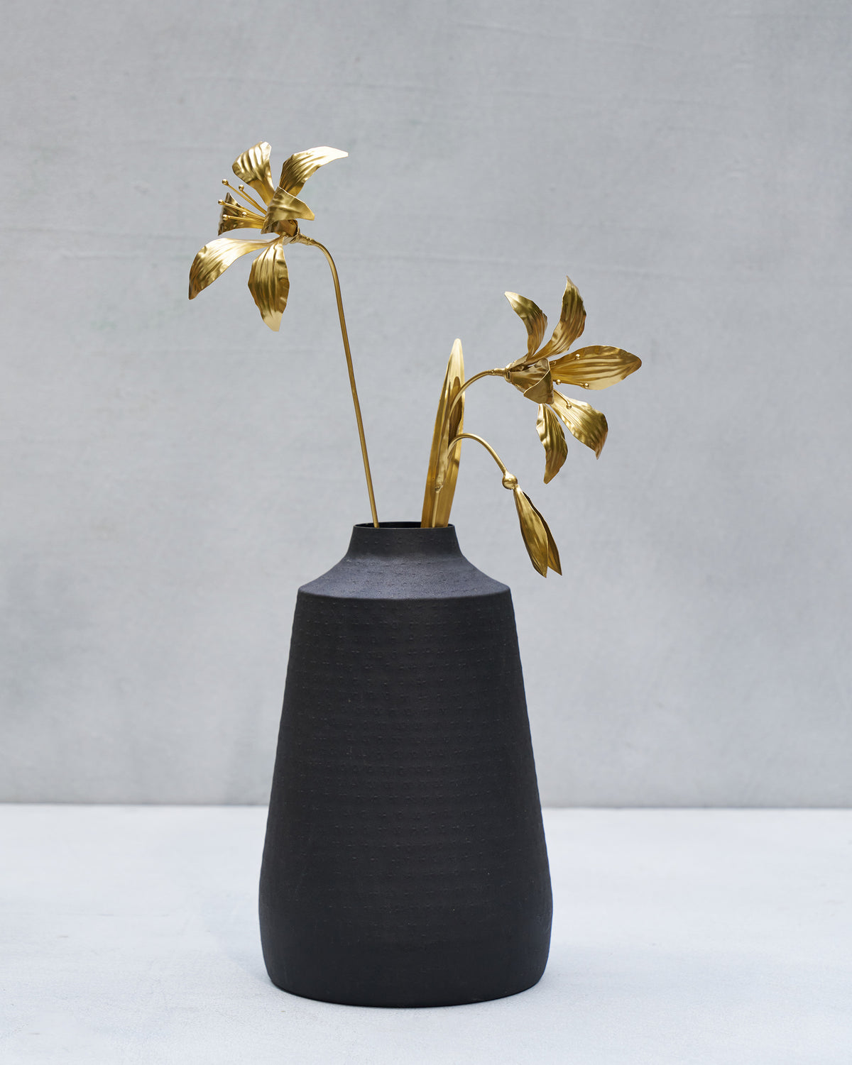 Gold Amaryllis accent stems with blooms and a bud in a black vase.