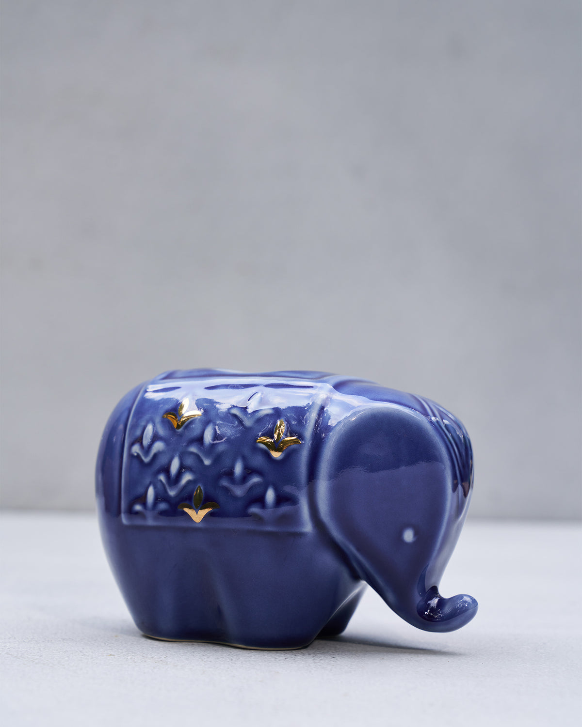 Side profile of a glossy blue Tusker elephant votive with gold accents.