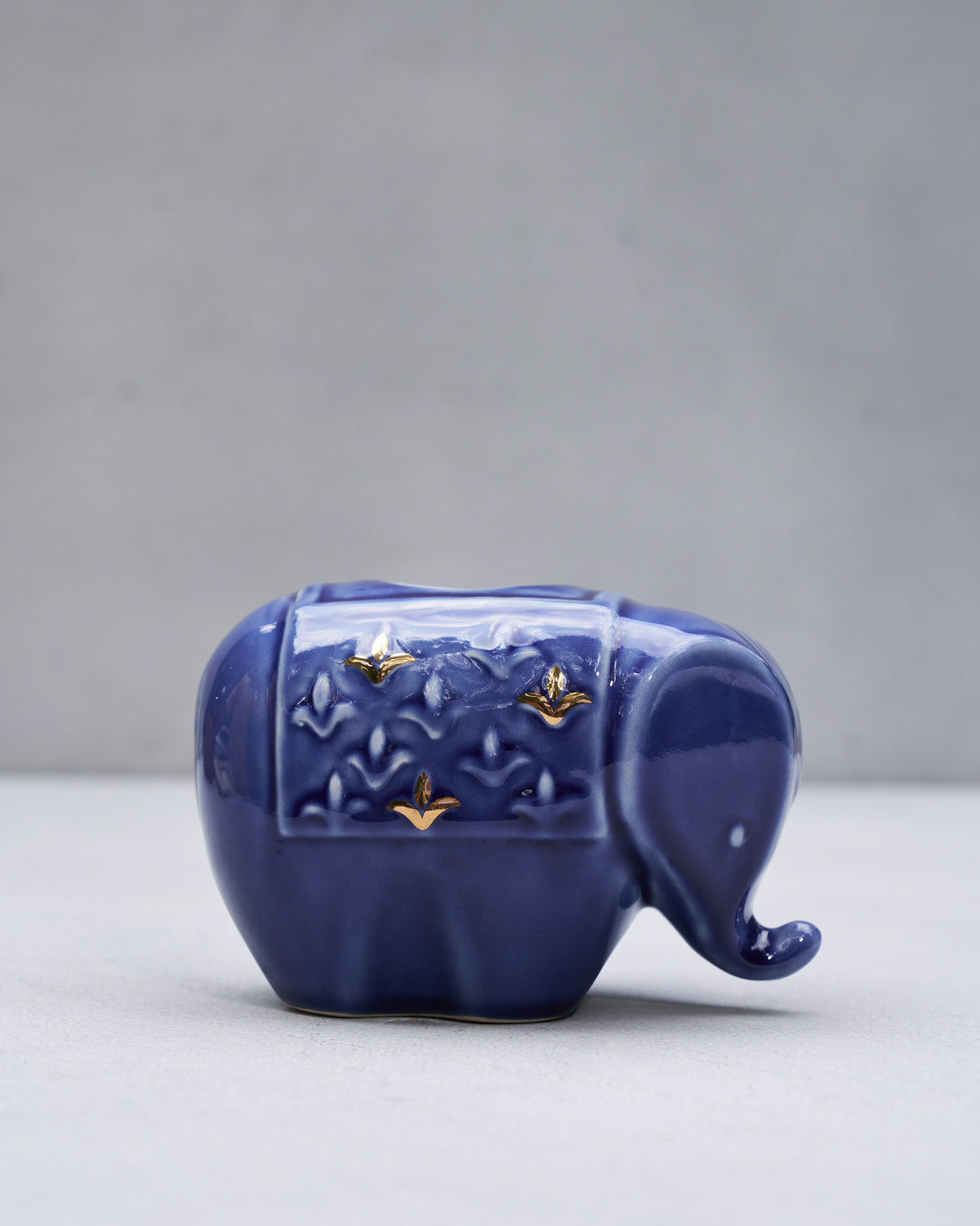Blue glazed Tusker elephant votive with gold motifs on a plain backdrop.