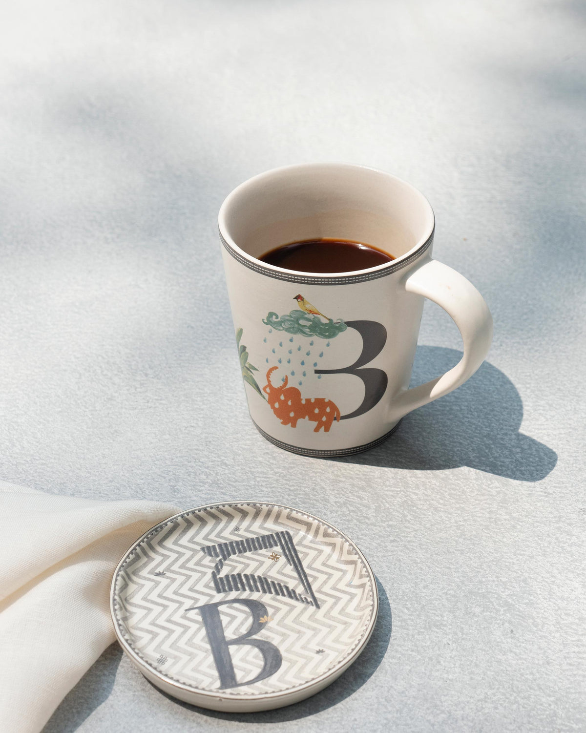 B Alphabet mug filled with coffee beside a matching letter B coaster.