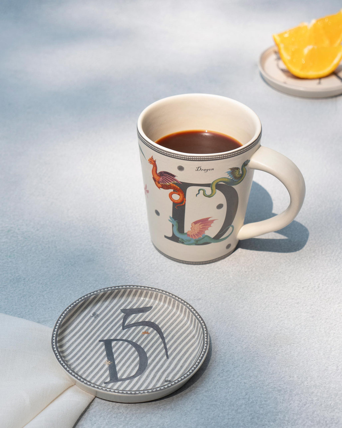 Letter D dragon mug with matching striped coaster and coffee.