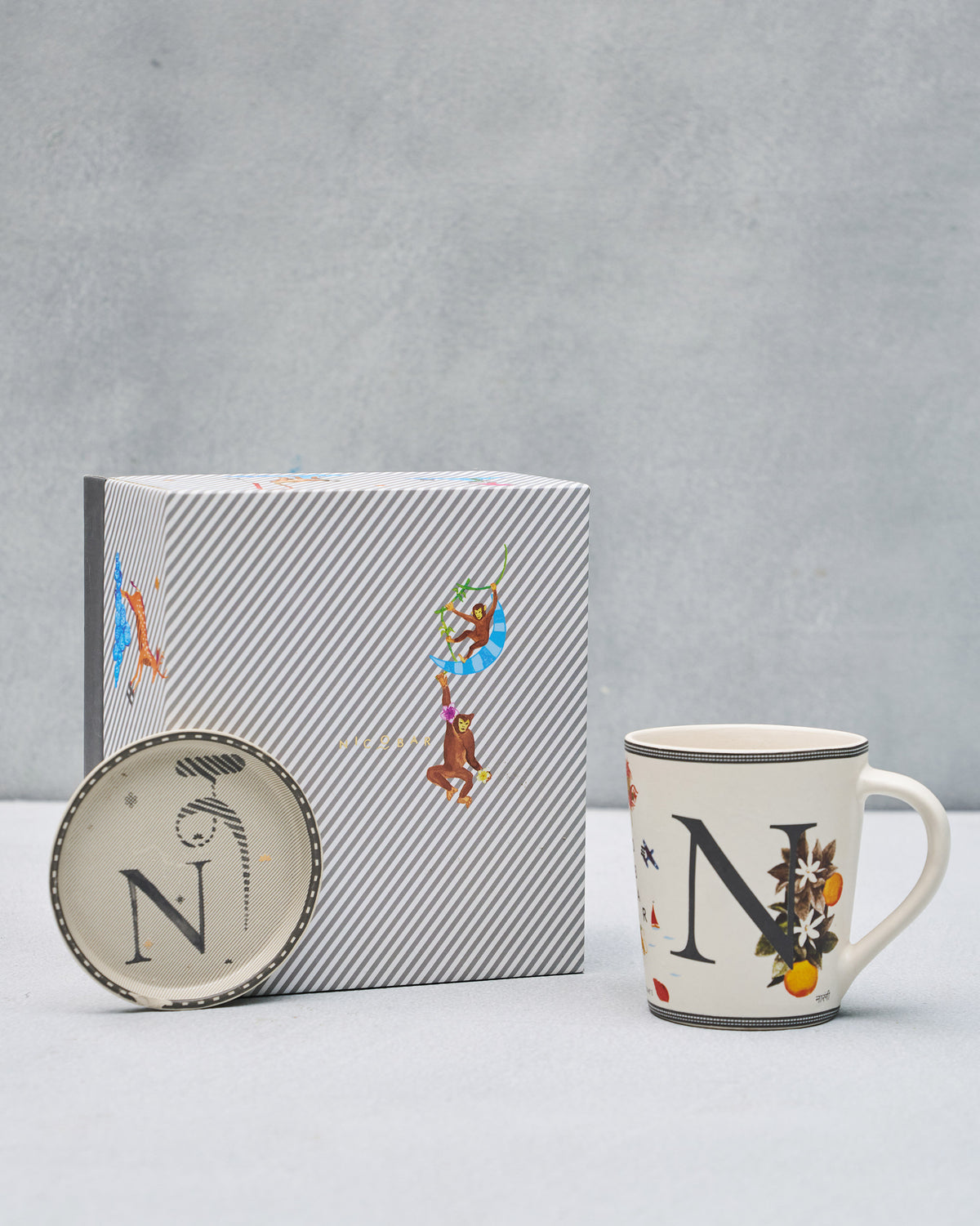 N alphabet mug and coaster set with citrus motifs beside its striped gift box.