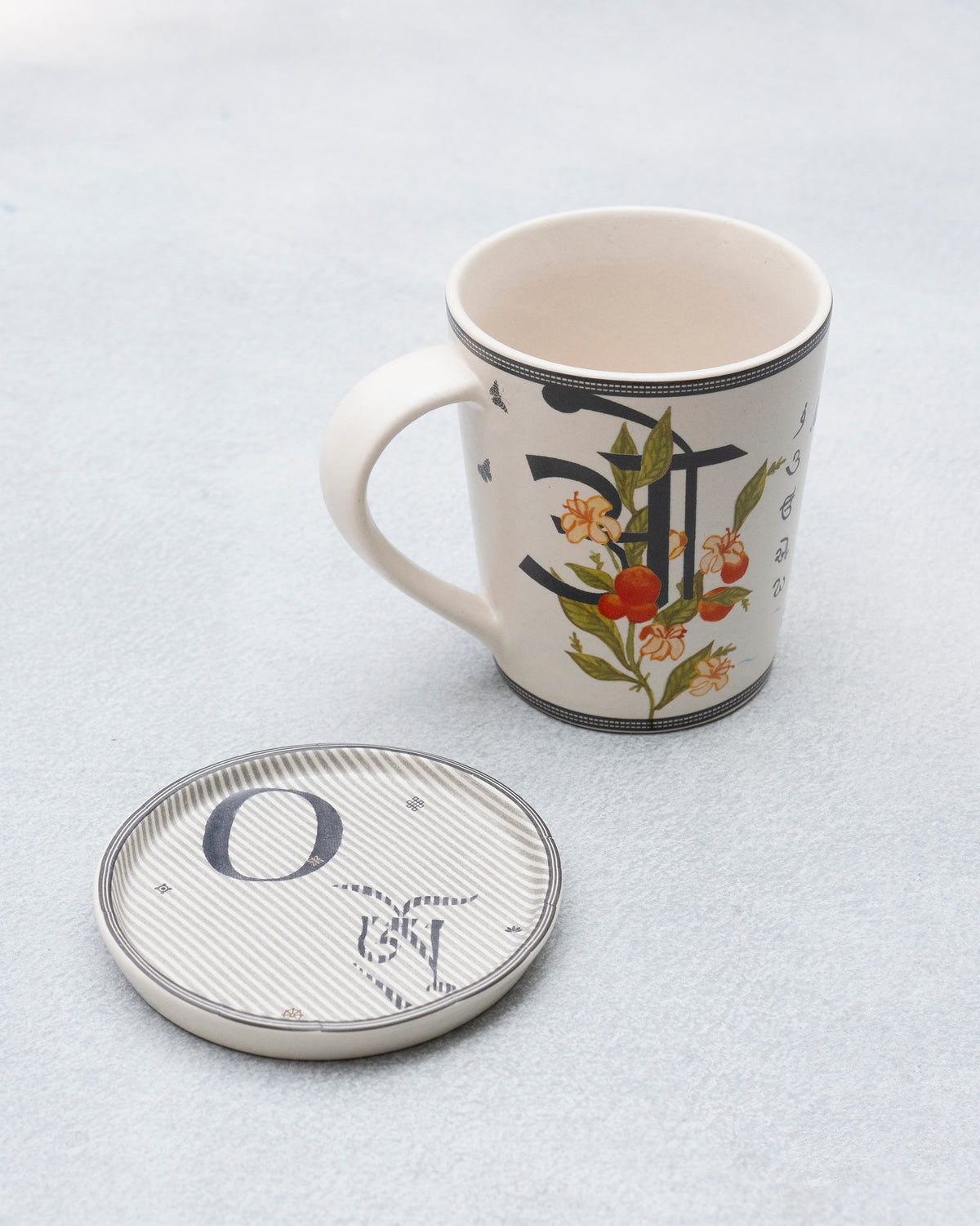 O alphabet mug with script and fruit print beside a striped letter O coaster.