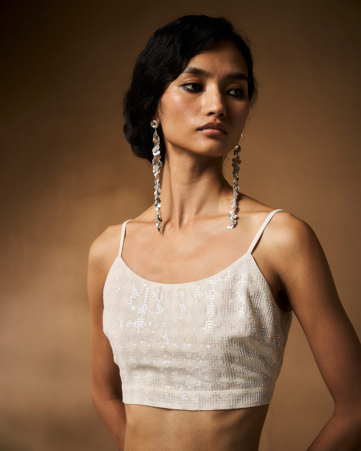 Person wearing an ivory sequined strappy cropped blouse.