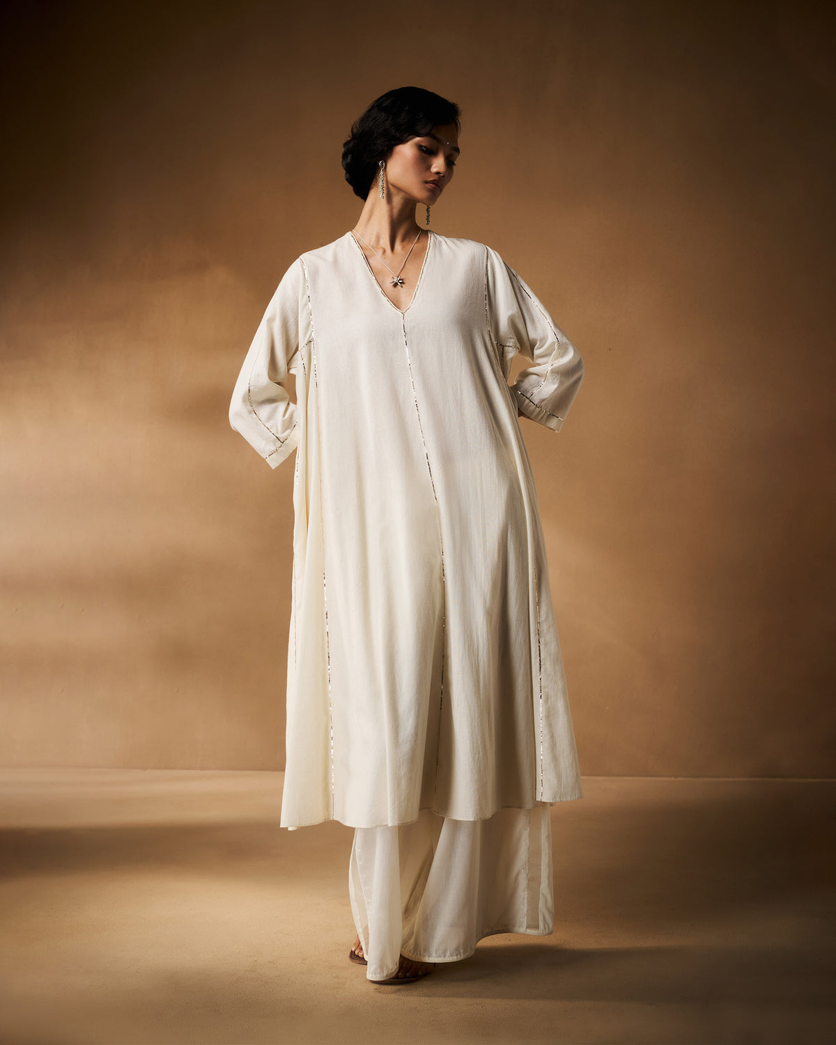 Person wearing an ivory Aheli Kurta with silver embroidered trim down the front.