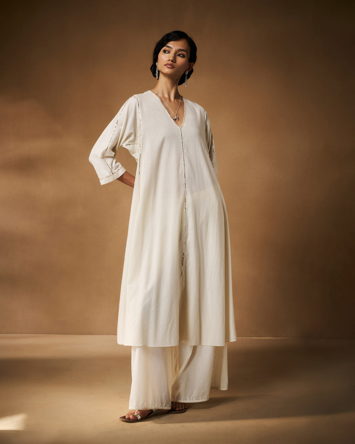 Person wearing a long ivory Aheli Kurta with silver embroidered seams.