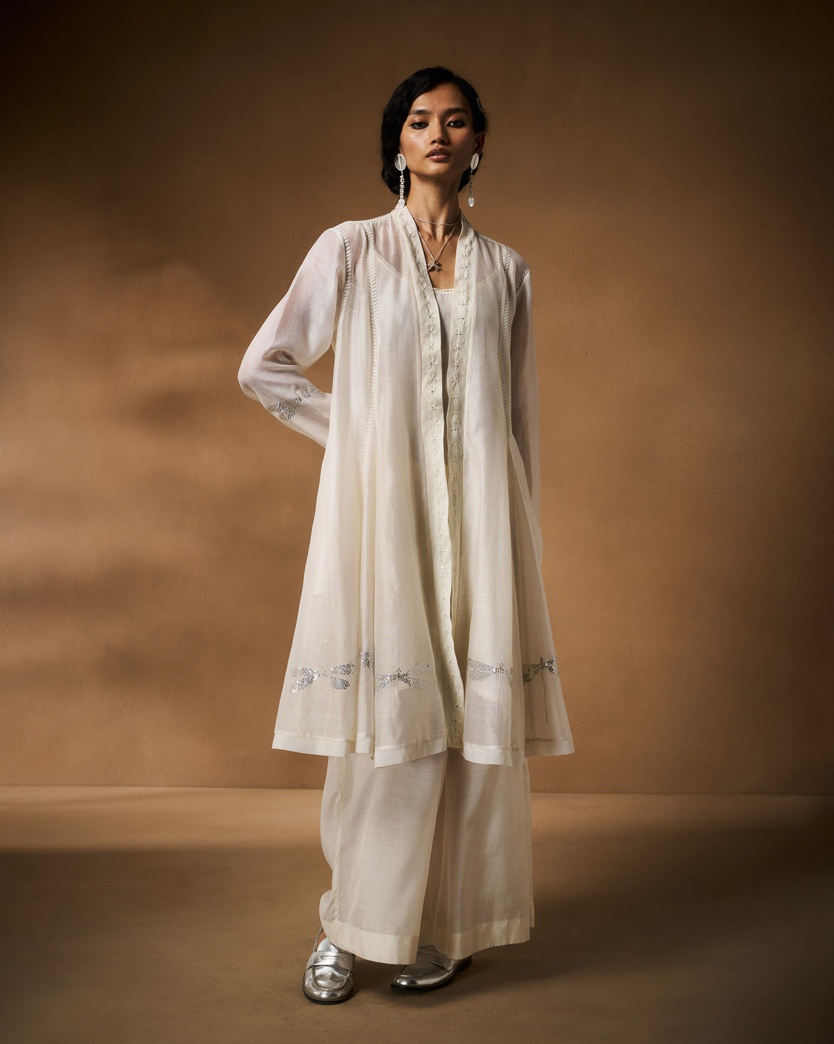 Person wearing an ivory Pavi overlay with silver dragonfly embroidery at the hem.
