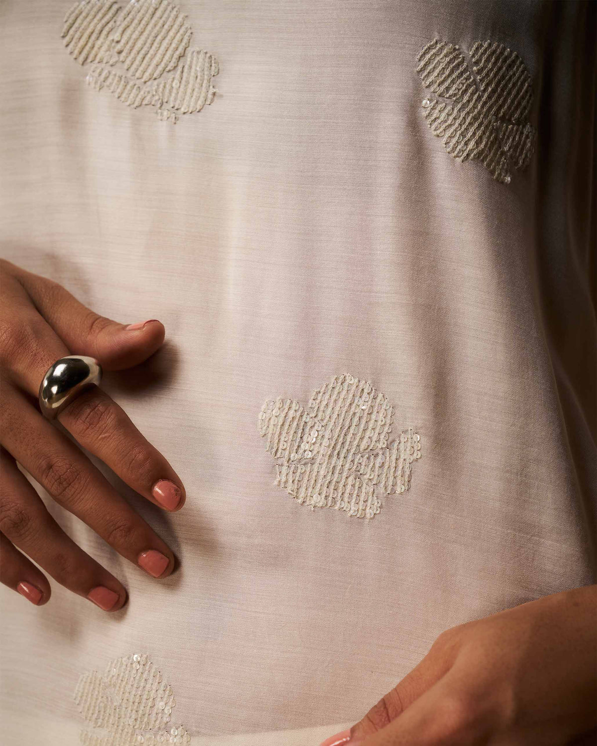 Close-up of an ivory camisole with raised floral embroidery and sequins.