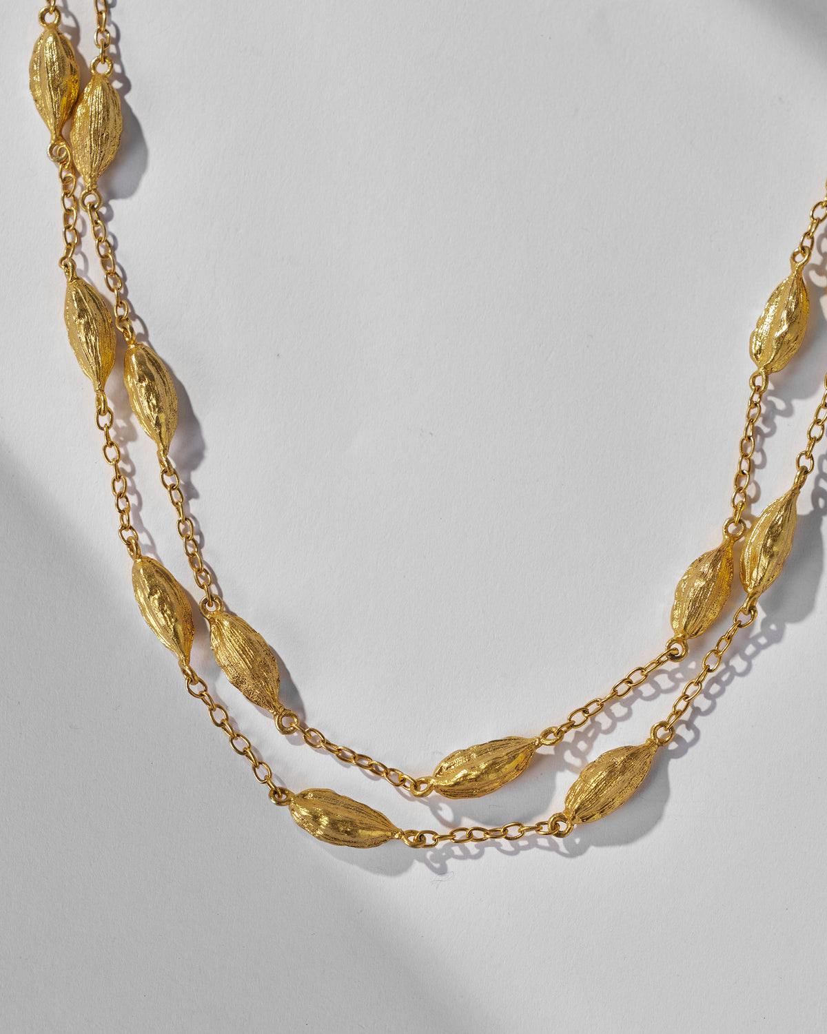 Close-up of gold Shanti Necklace showing its textured oval beads on two chain strands.