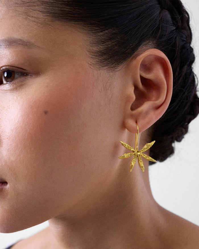 Side profile of a gold Star Anise dangle earring on a person.