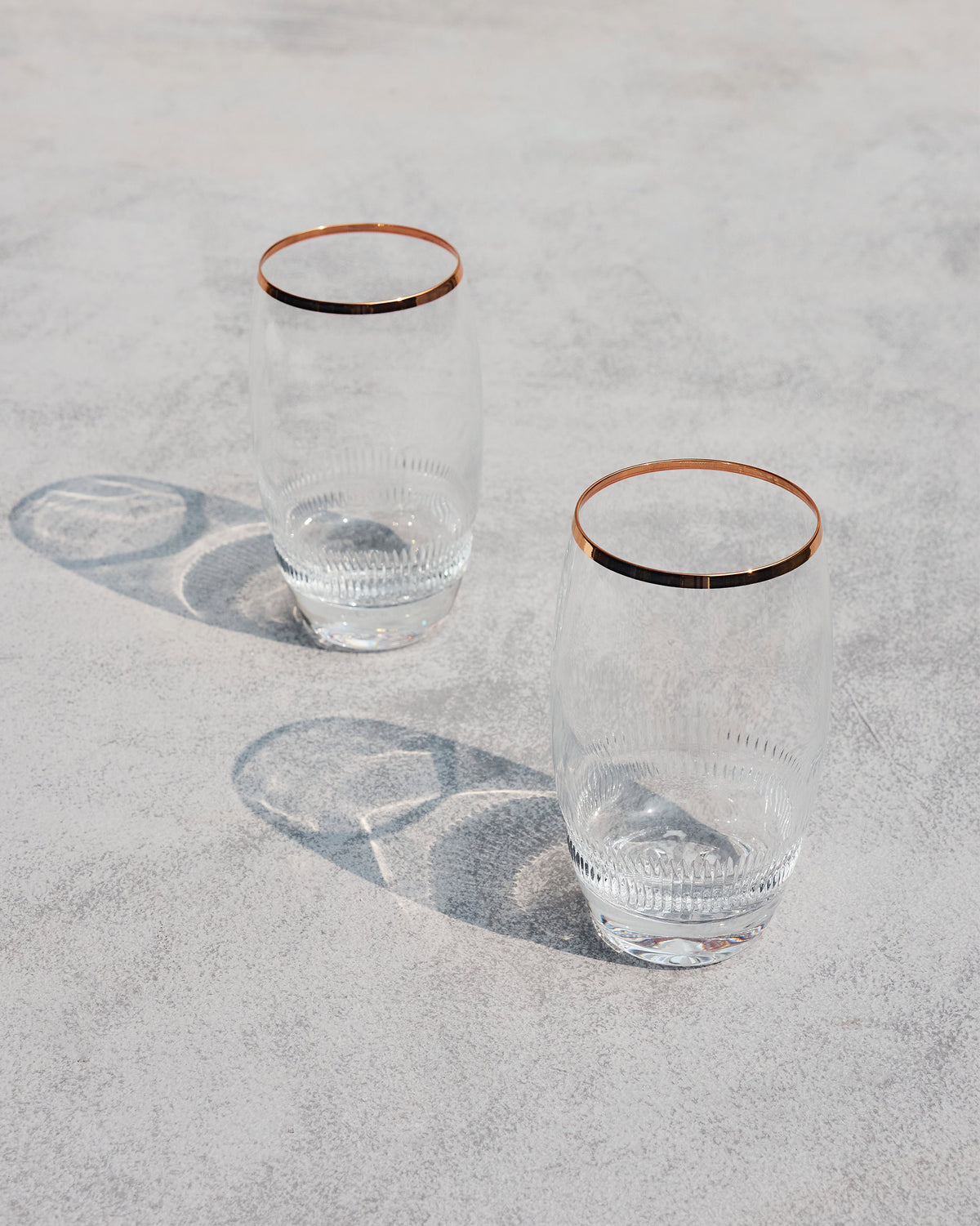 Serena highball glasses with copper rims standing on a stone surface.