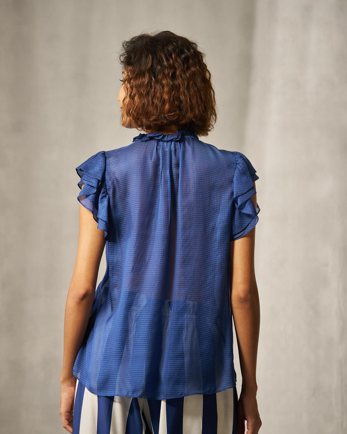 Back of a blue check shirt with ruffled sleeves and a high ruffle collar.