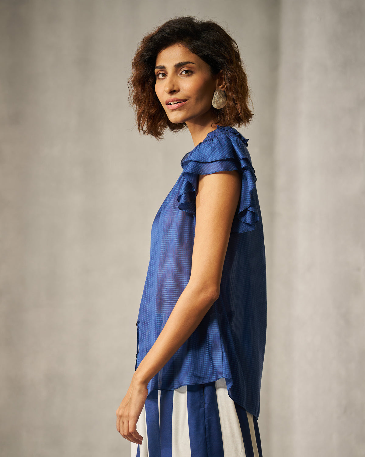 Side view of a blue check shirt with tiered ruffle sleeves.