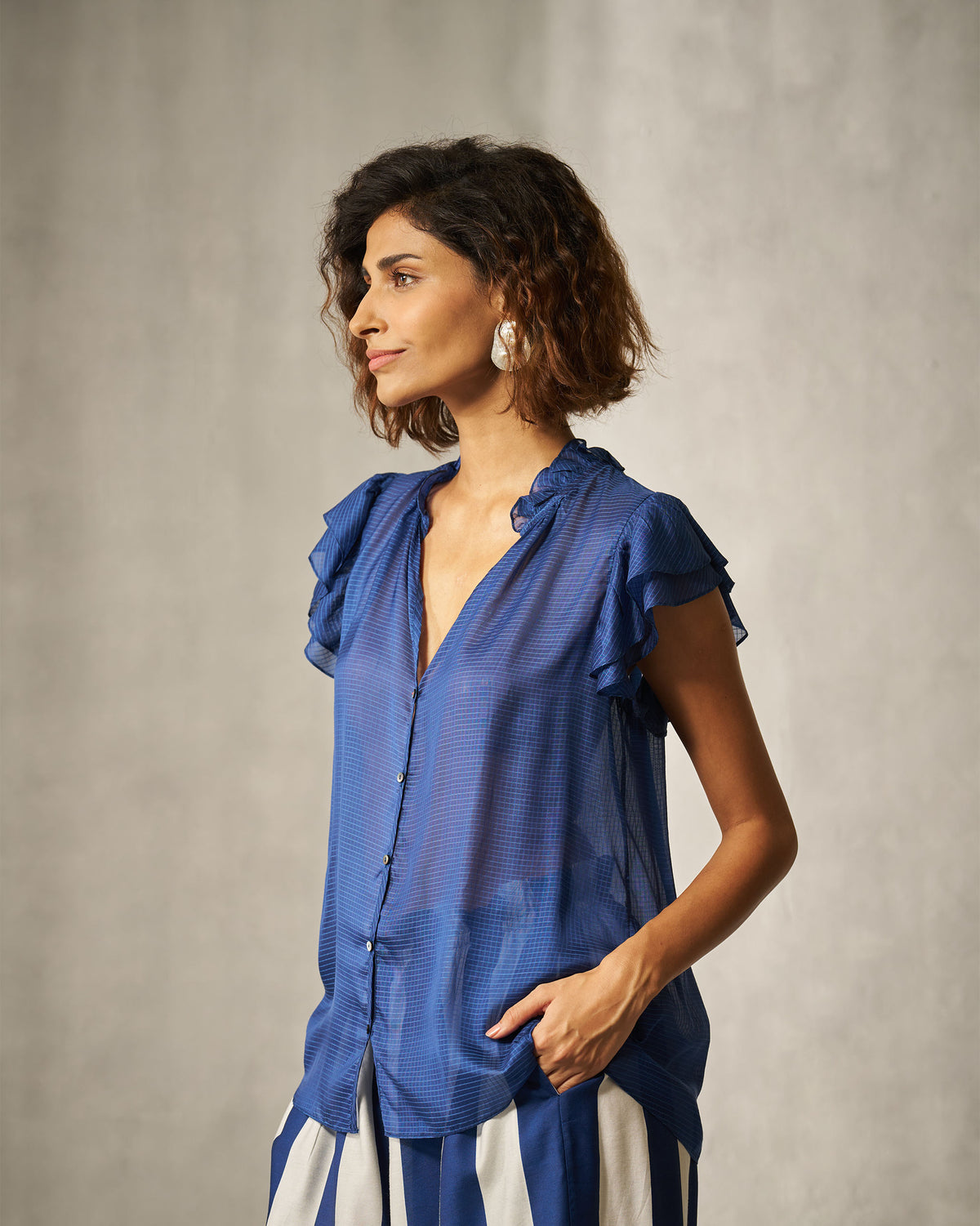 Person wearing a blue check shirt with a ruffled collar and short sleeves.