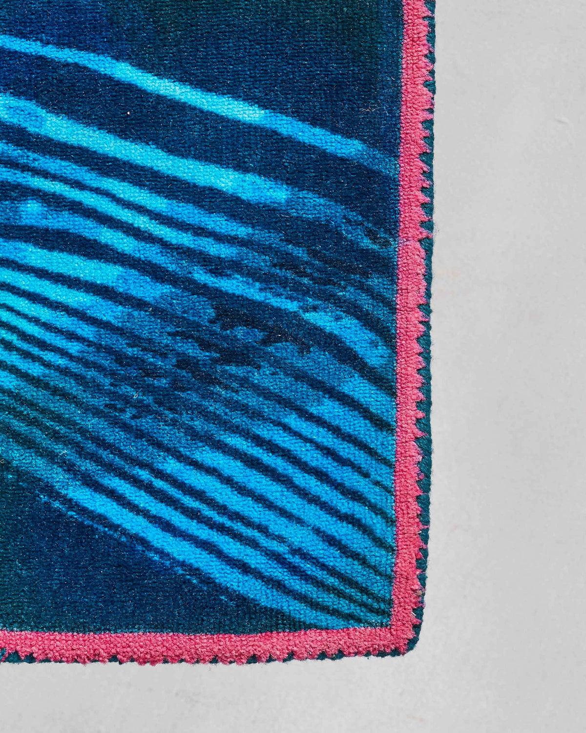 Close-up of a Pacific rug corner showing its pink border and wave lines.