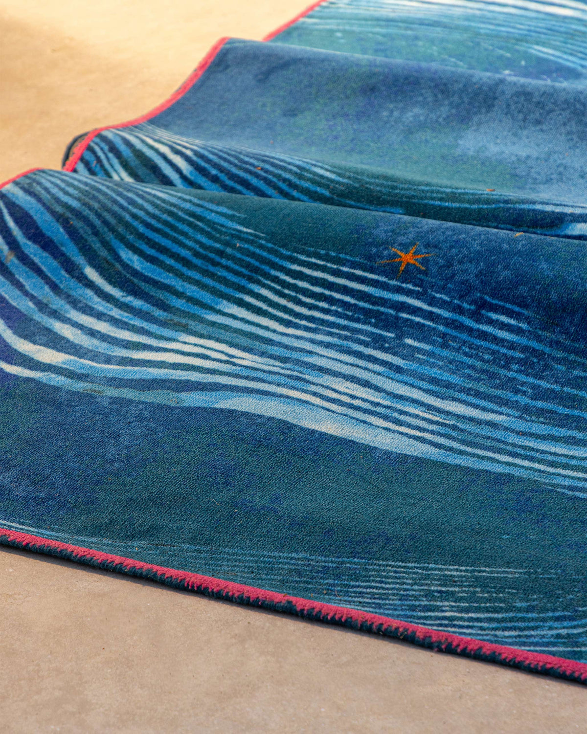 Pacific rug curled at an angle, showing an orange star motif.