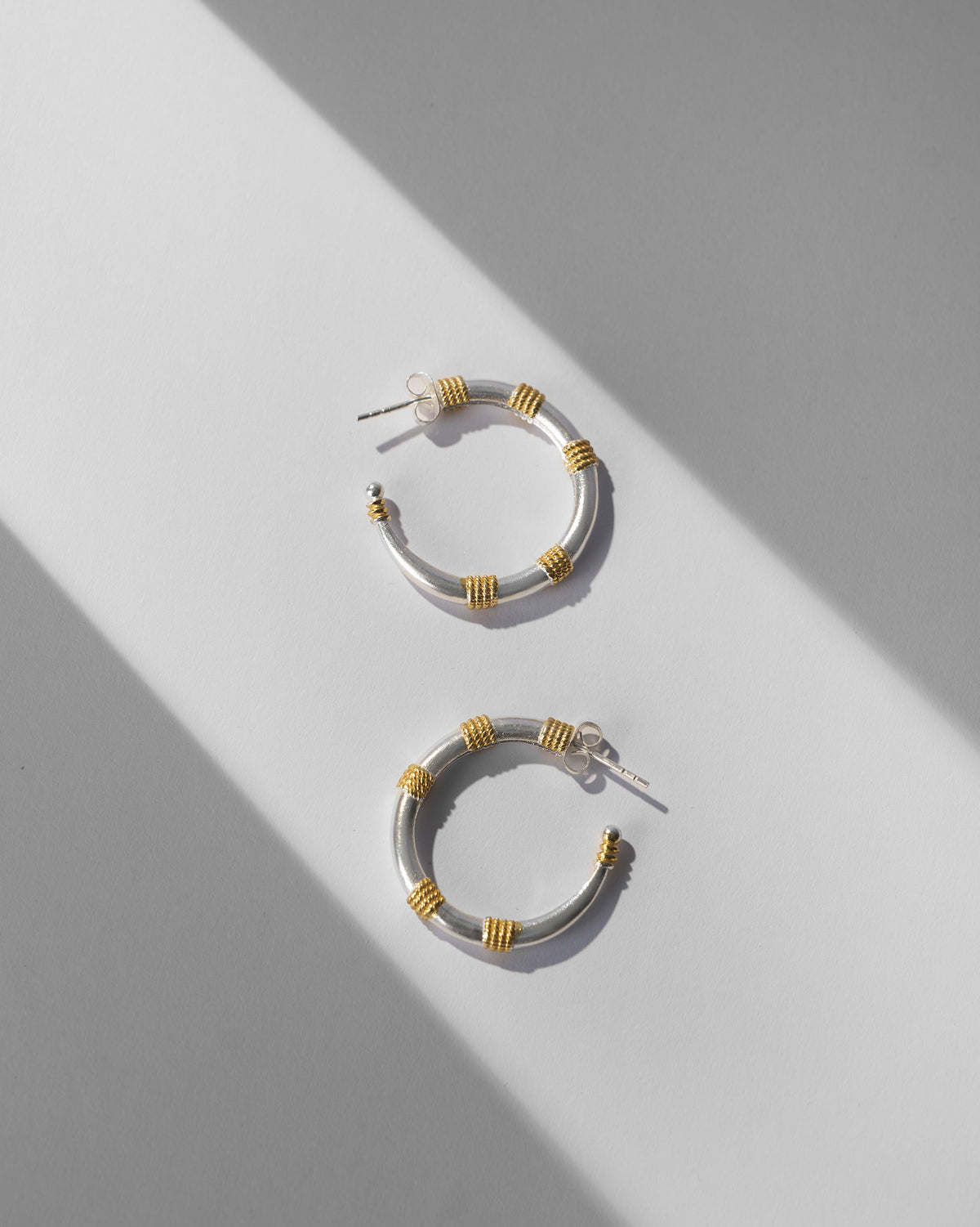 Pair of small silver and gold dhoop chaon hoops laid flat.