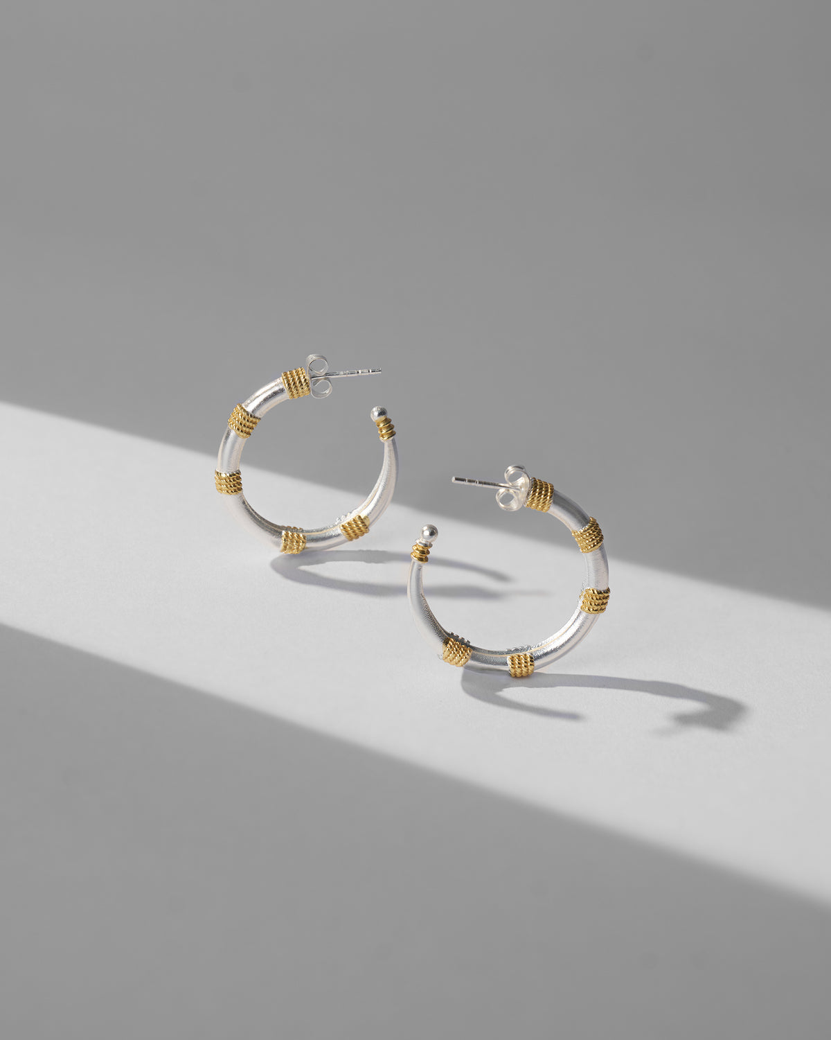 Silver and gold dhoop chaon hoops showing tubular form and gold wraps.