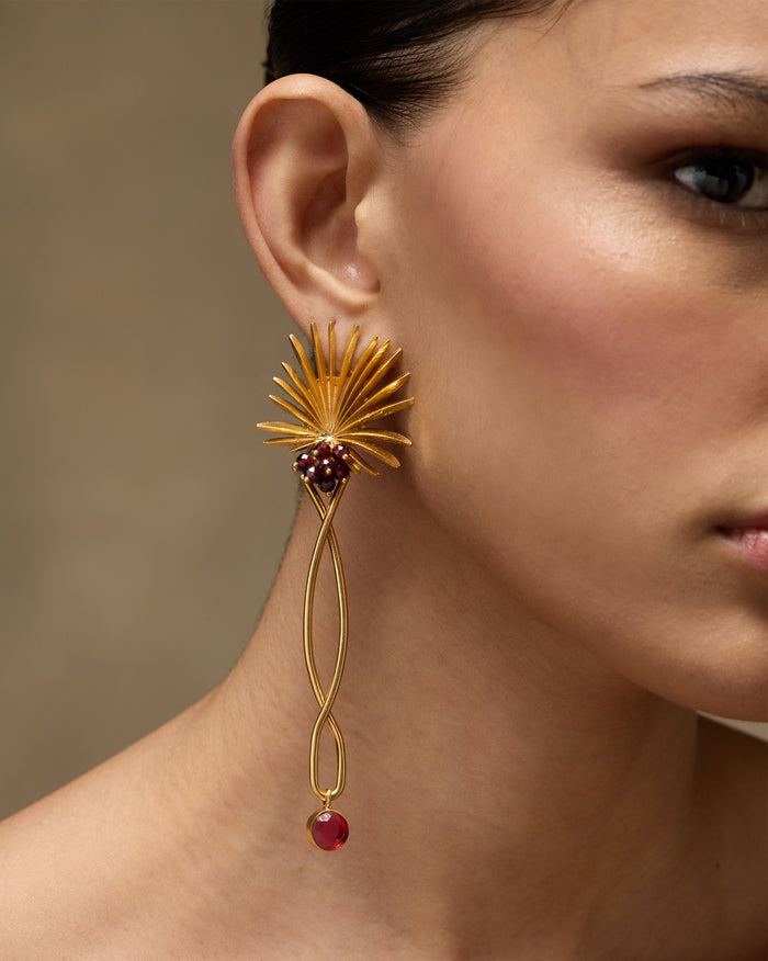 Side view of gold Palm Danglers worn on a person, showing the red drop.