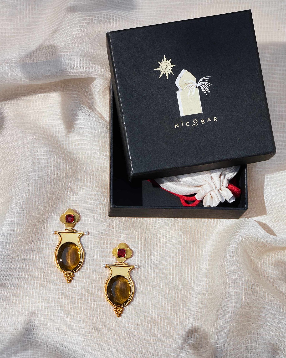 Gold eden drop earrings beside a black Nicobar gift box.
