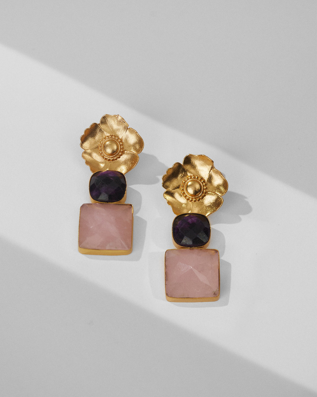 Pair of gold dessert rose ruby drops with pink stones laid flat.