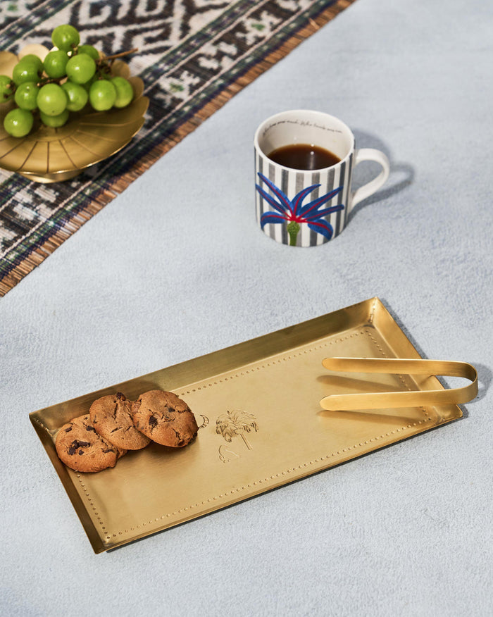 Gold Sahara cookie tray with tongs holding cookies beside a coffee mug.
