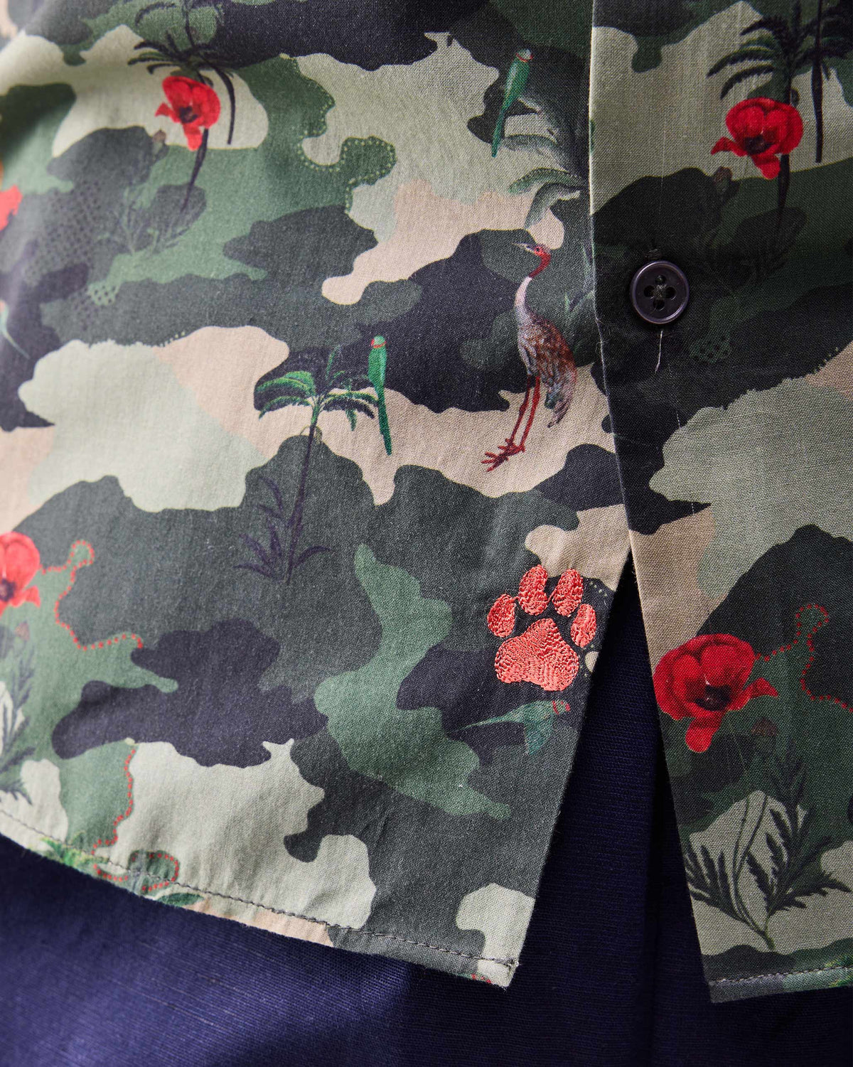 Close-up of rust paw embroidery near the hem of a dark green Hakuna shirt.
