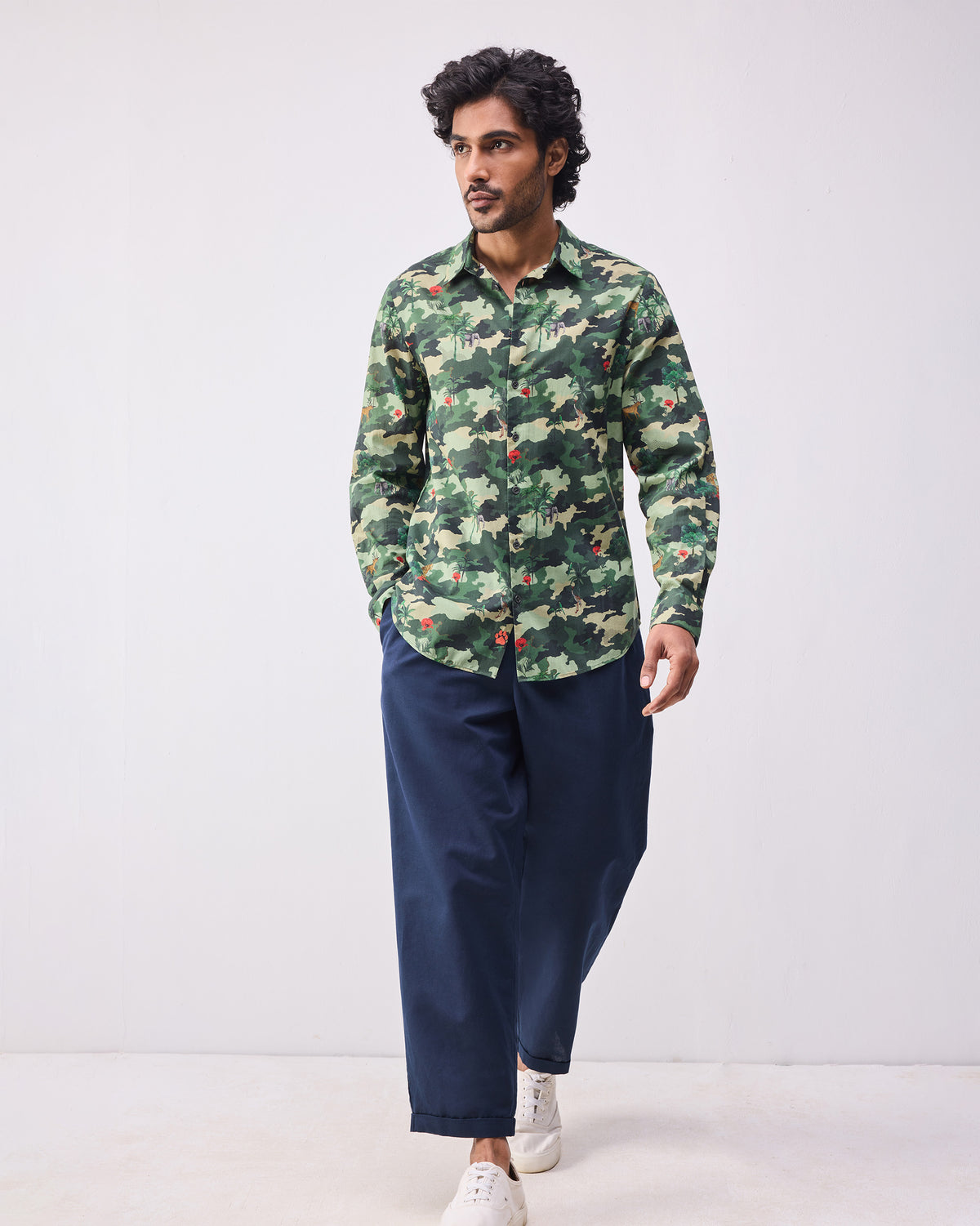 Person wearing a dark green camo Hakuna shirt untucked over navy trousers.