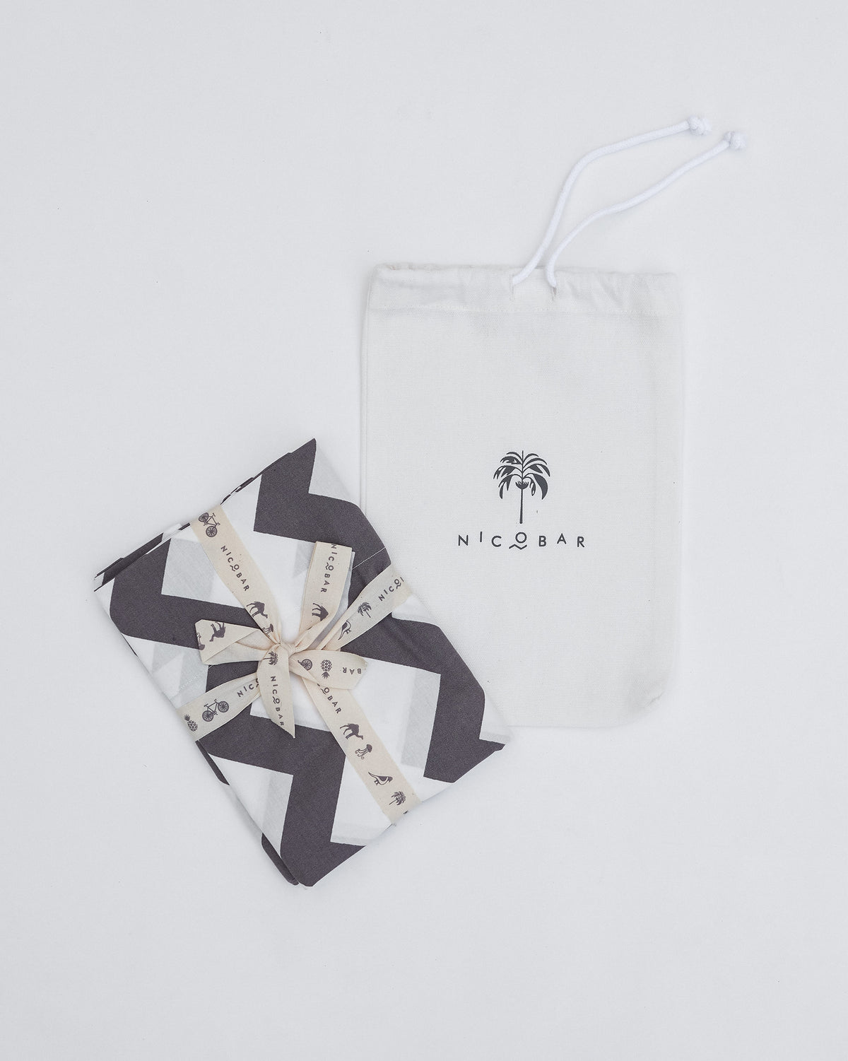 Folded grey and white Colombo Wave bedsheet with a Nicobar pouch.