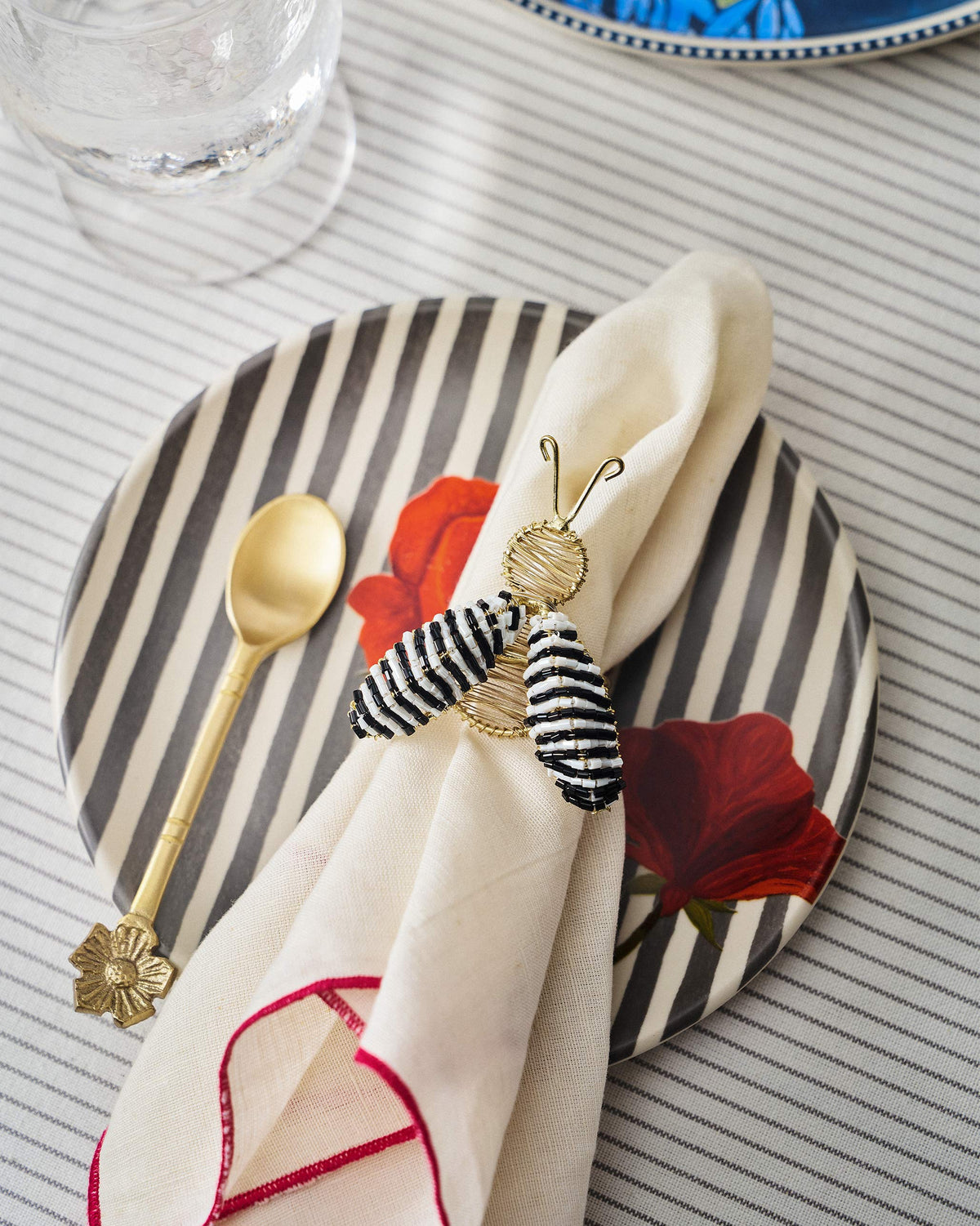 Gold-wire bee napkin ring with striped wings holding a cream linen napkin.