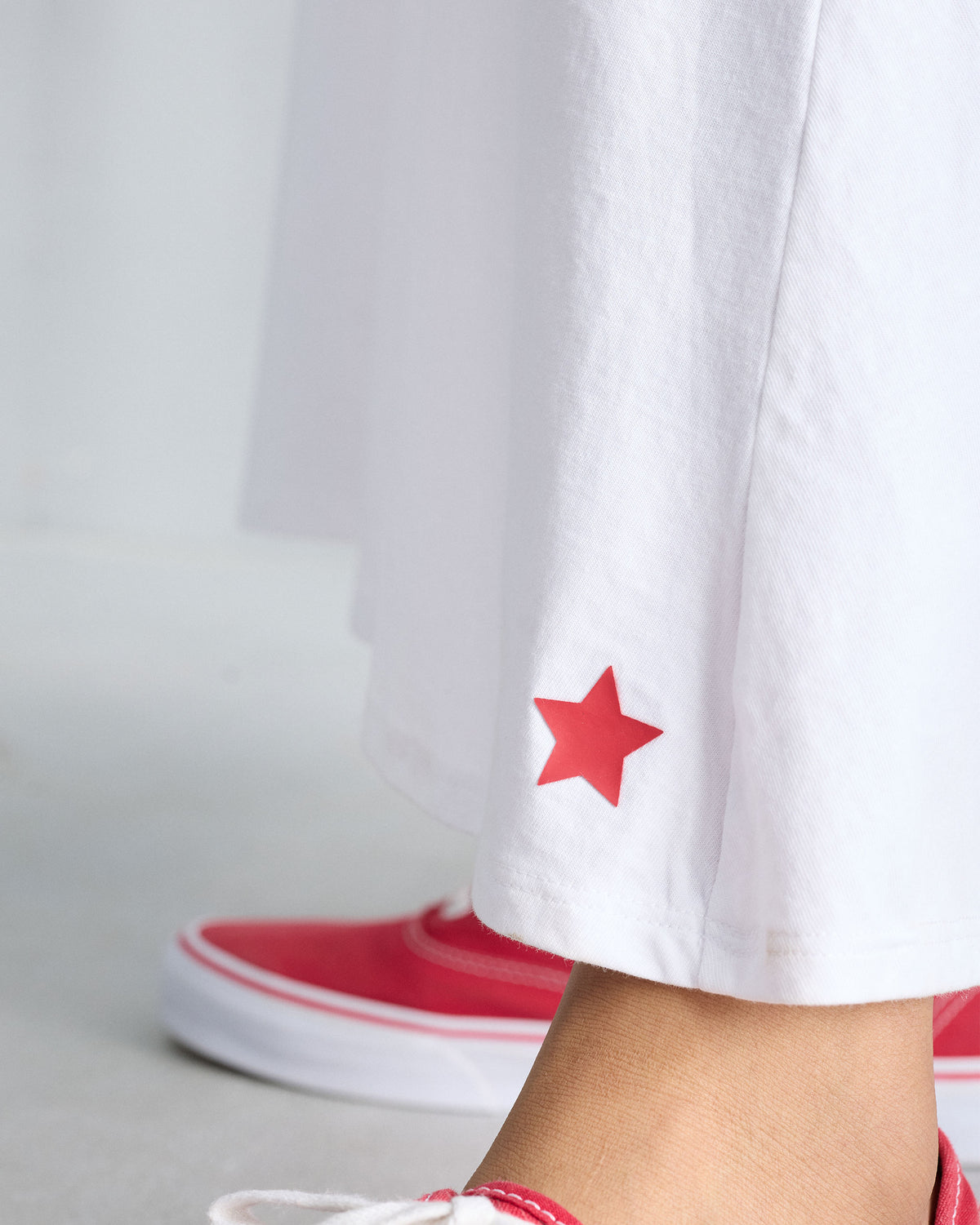 Close-up of a red star near the hem of a white Esther dress.