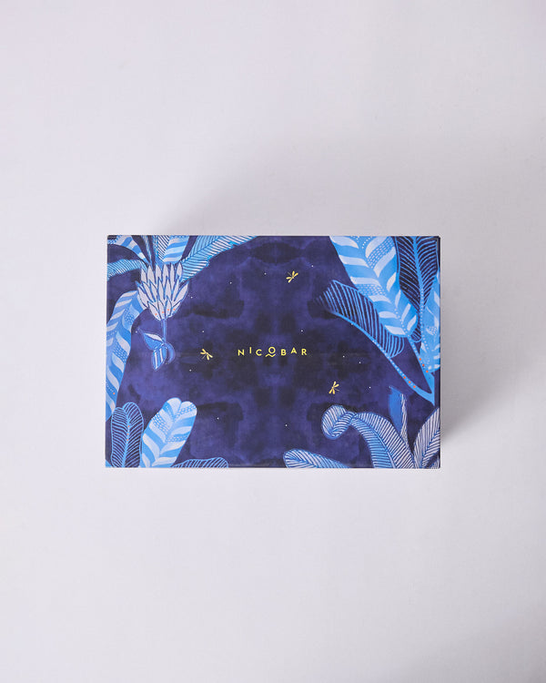 The closed navy gift box, covered in blue tropical leaves