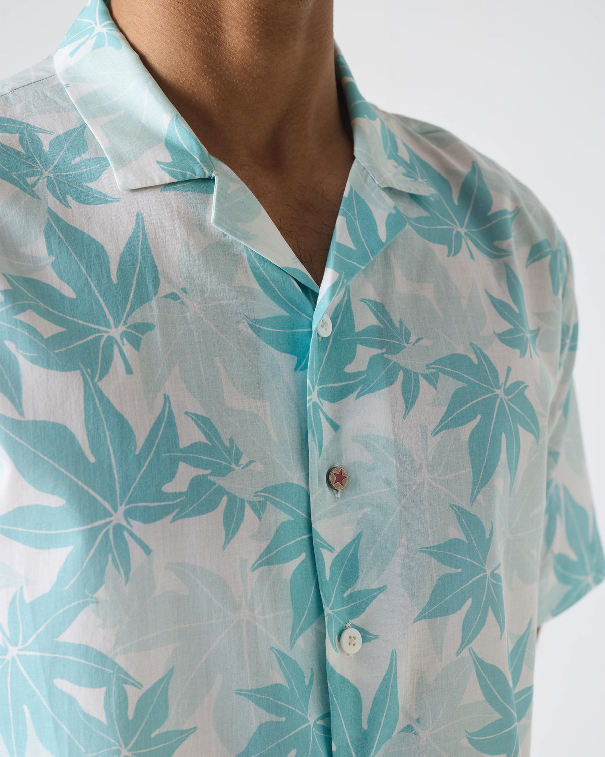Close-up of a Mistari shirt showing teal leaf print and a red star button.